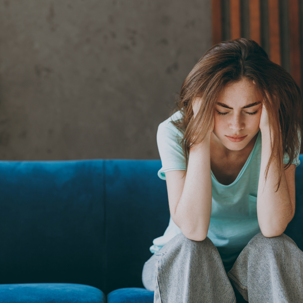 Young woman with Sjogren's disease sits with her head in her hands, looking tired